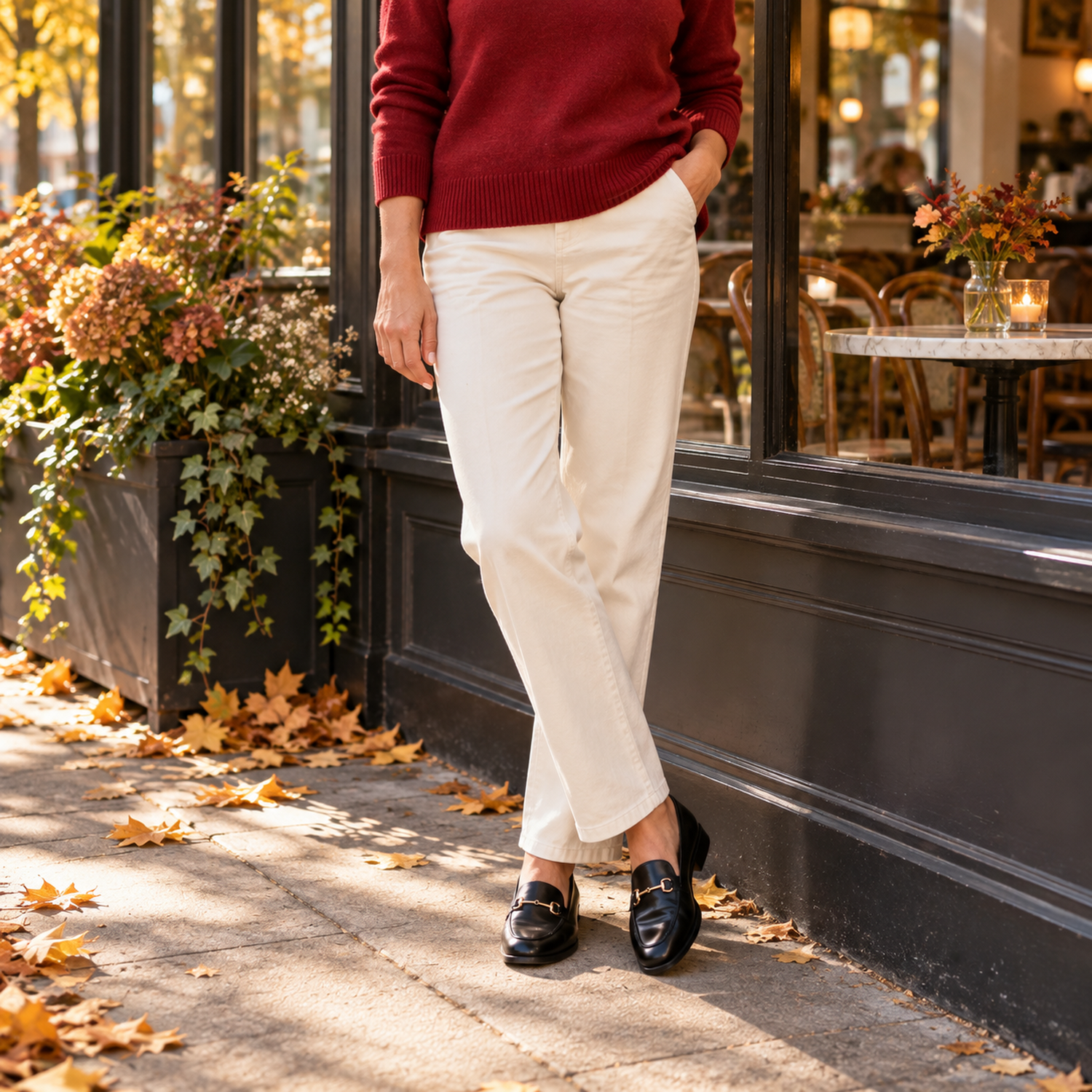 Cranberry red sweater styled with cream trousers and black loafers beside a cafe window