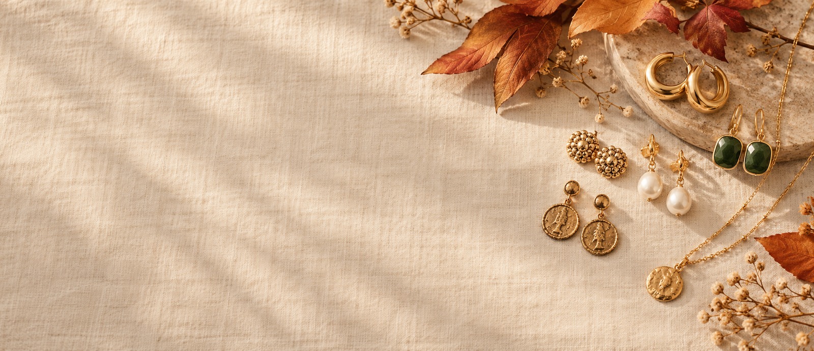 Flat lay of assorted earrings and a necklace on cream linen with dried autumn leaves, styling illustration